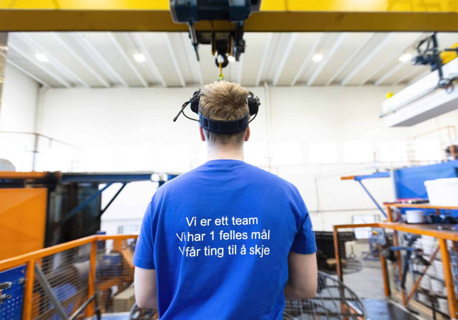 The back of a man working in the factory. Text on the back of his blue t-shirt reads "We are one team. We have one common goal. We make things happen."
